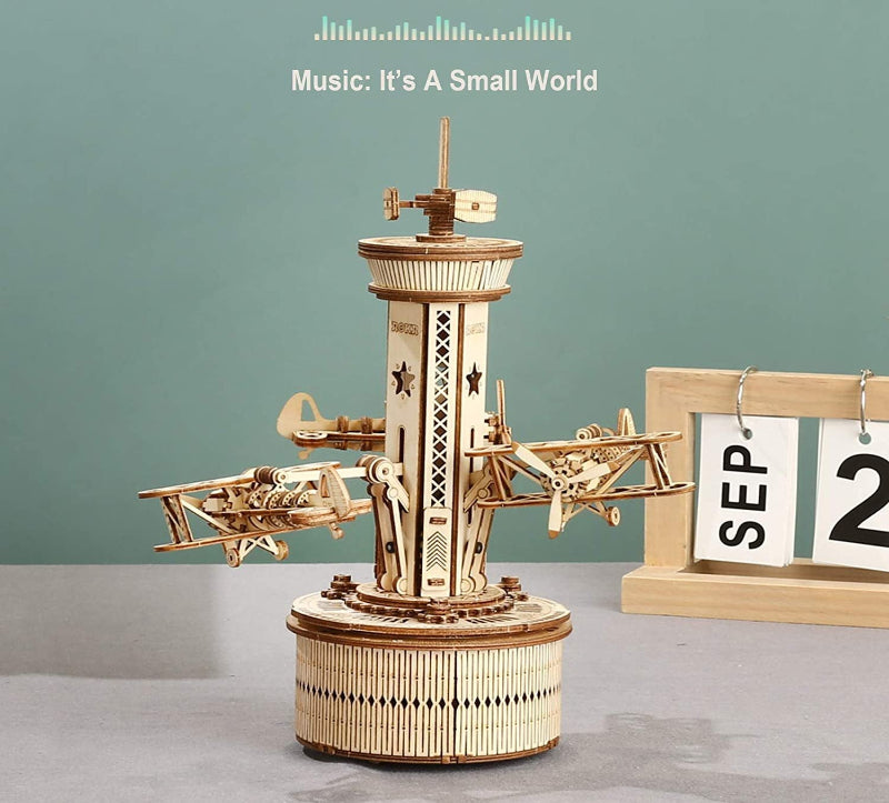 Wooden mechanical model with music player on a gray surface against a green background