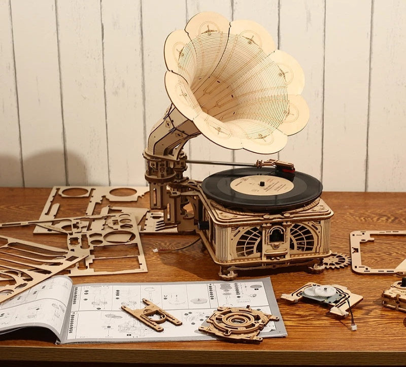 Wooden gramophone model kit on a wooden table with instructions and unassembled parts.