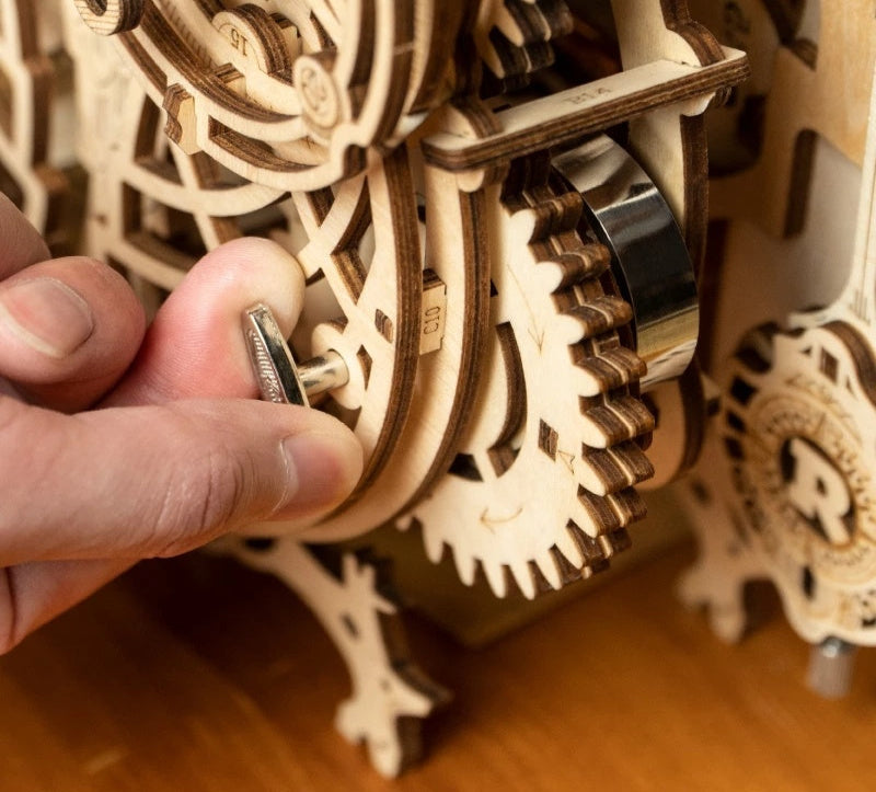 Hand interacting with a wooden mechanical model of gears on a wooden surface