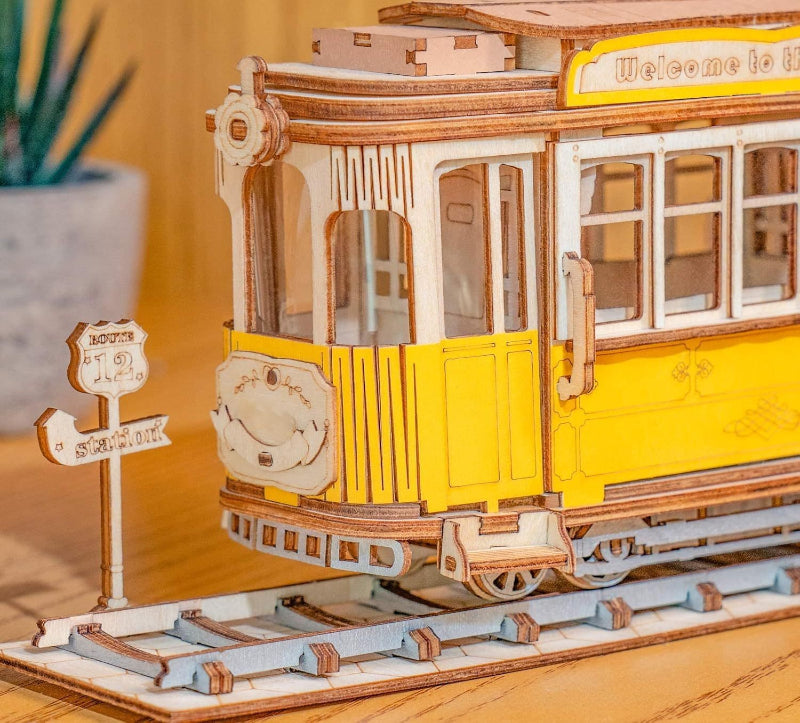 Wooden model of a tram with yellow body and brown roof on a wooden surface.